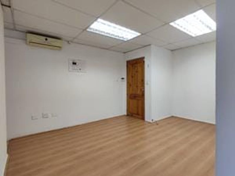 An empty bedroom featuring laminate flooring, a suspended ceiling with recessed lighting, and a wall-mounted air conditioning unit.