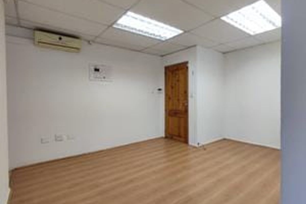 An empty bedroom featuring laminate flooring, a suspended ceiling with recessed lighting, and a wall-mounted air conditioning unit.