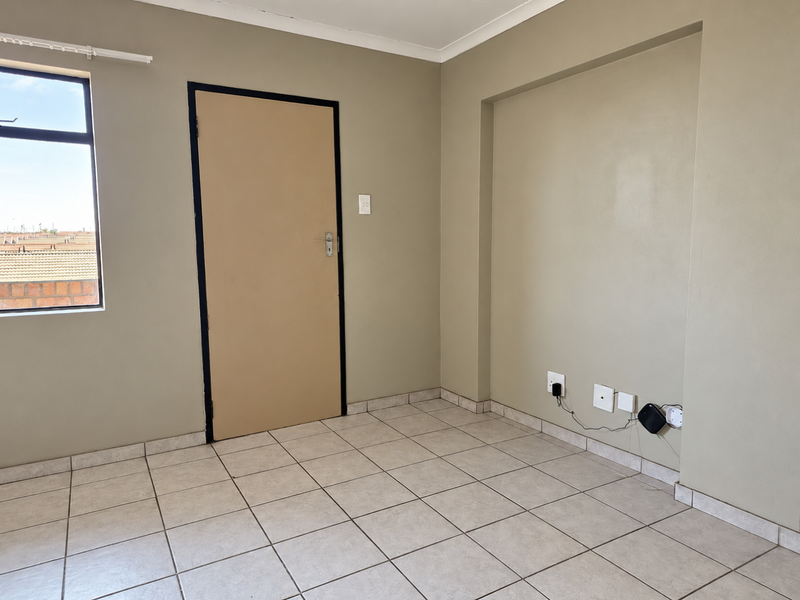 An empty bedroom featuring neutral wall paint, tiled flooring, a built-in wall niche, and a window providing natural light.