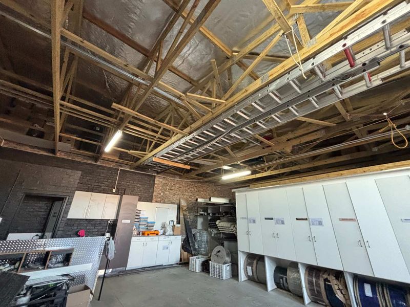 A functional utility or storage space featuring exposed timber roof trusses, reflective insulation, built-in cabinetry, and exposed brick walls.
