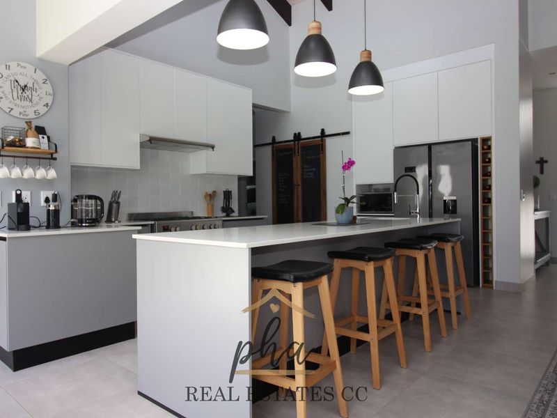 Modern open-plan kitchen featuring sleek white cabinetry, a central island with breakfast bar, stone countertops, and integrated stainless steel appliances.