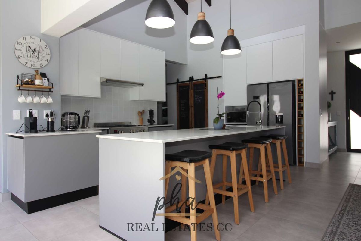 Modern open-plan kitchen featuring sleek white cabinetry, a central island with breakfast bar, stone countertops, and integrated stainless steel appliances.