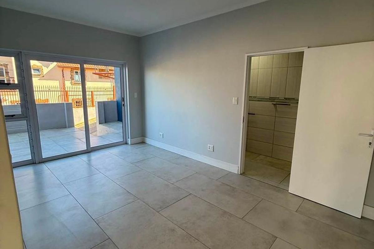 A bright, empty bedroom featuring large format floor tiles, a sliding glass door leading to a patio, and an attached en-suite bathroom.