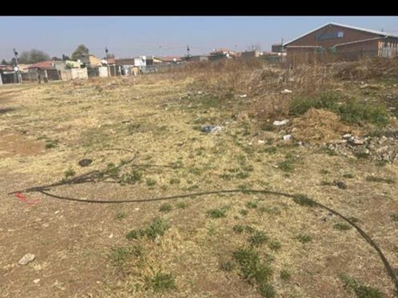 A vacant residential plot of land featuring dry grass and scattered debris, offering a blank canvas for future development.