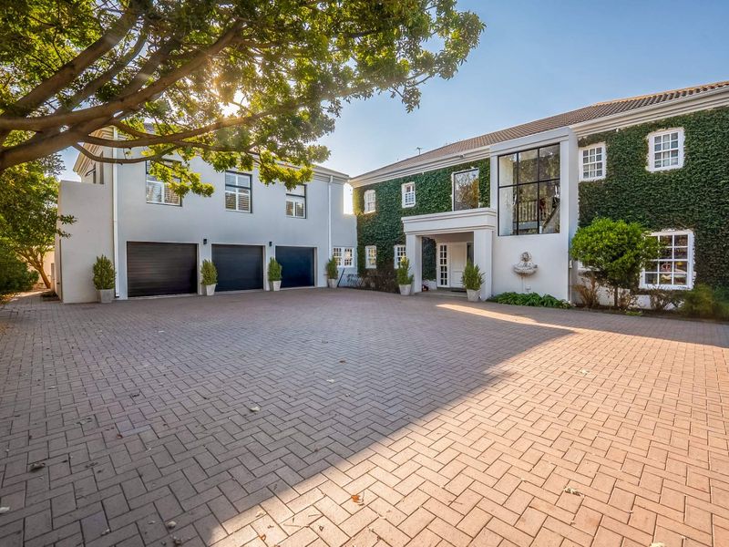 Impressive front elevation featuring a spacious paved driveway, triple garage, and a striking facade adorned with climbing ivy and a classic wall fountain.