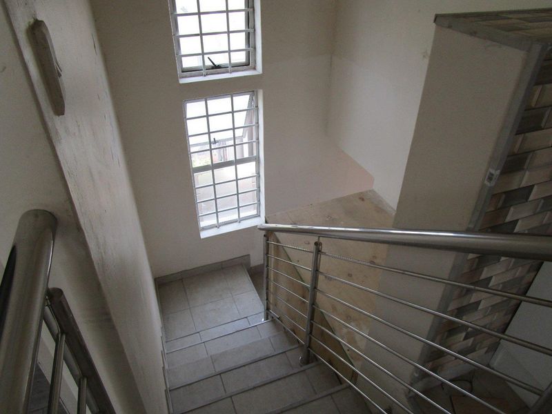 A staircase area featuring tiled steps, a stainless steel balustrade, and windows with security bars, currently showing signs of wear and unfinished wall surfaces.