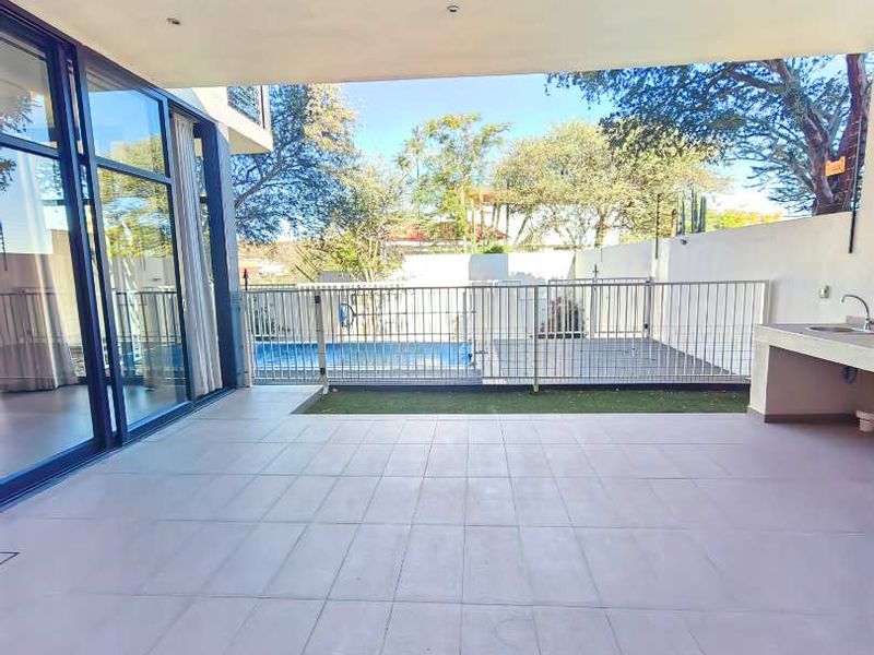 Spacious covered patio featuring tiled flooring, a built-in outdoor sink, and seamless access to the pool area through large sliding glass doors.