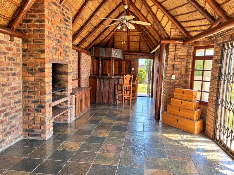 Spacious covered patio featuring a thatched roof, built-in braai, and a rustic bar area, perfect for outdoor entertaining with durable slate tile flooring.