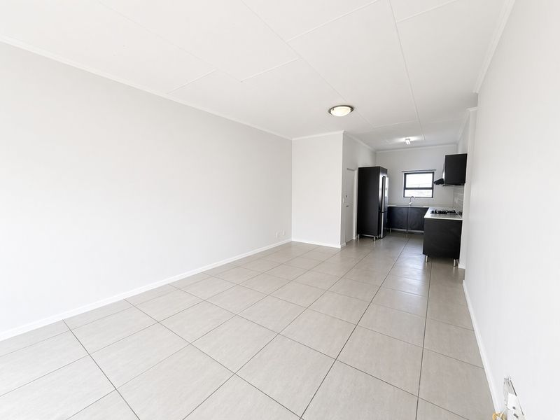An open-plan living and kitchen area featuring neutral tiled flooring, modern dark cabinetry, and a clean, minimalist aesthetic ready for personalization.