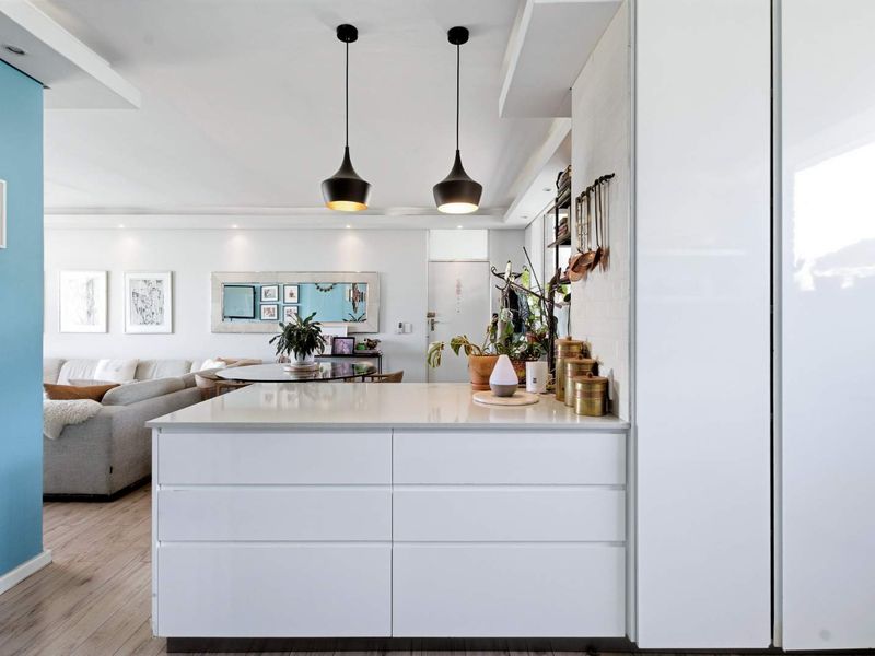 Modern open-plan living area featuring a sleek kitchen island with quartz countertops, pendant lighting, and light-toned laminate flooring throughout the space.