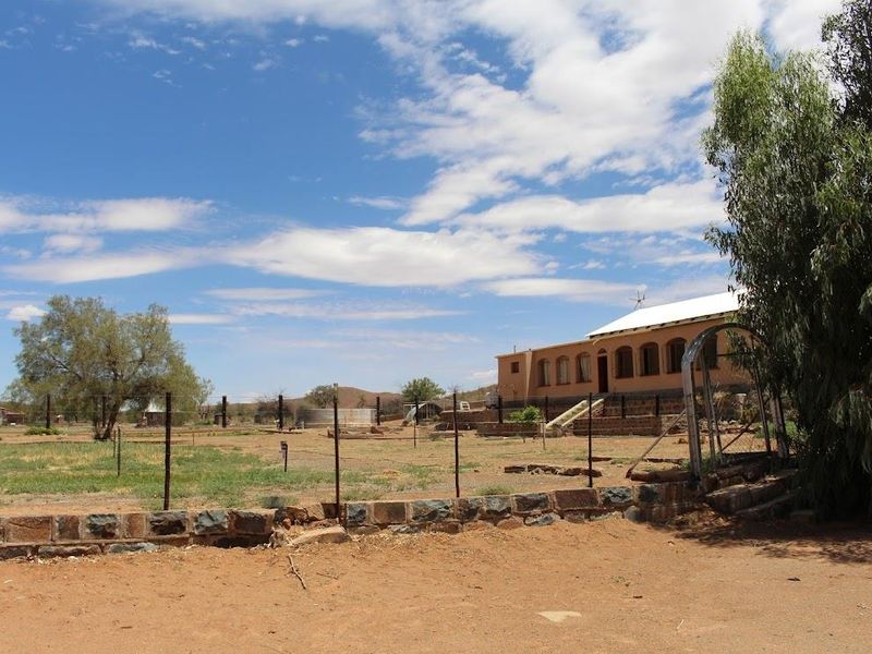 A wide view of the farm property featuring a single-story dwelling with a covered veranda, set within a large, open, fenced landscape.