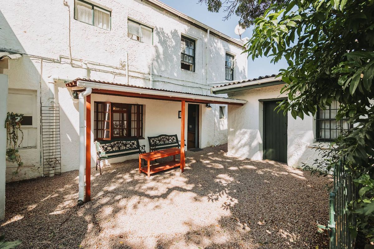 A rear exterior view featuring a covered patio area with gravel flooring, timber support posts, and traditional casement windows set against a white rendered facade.