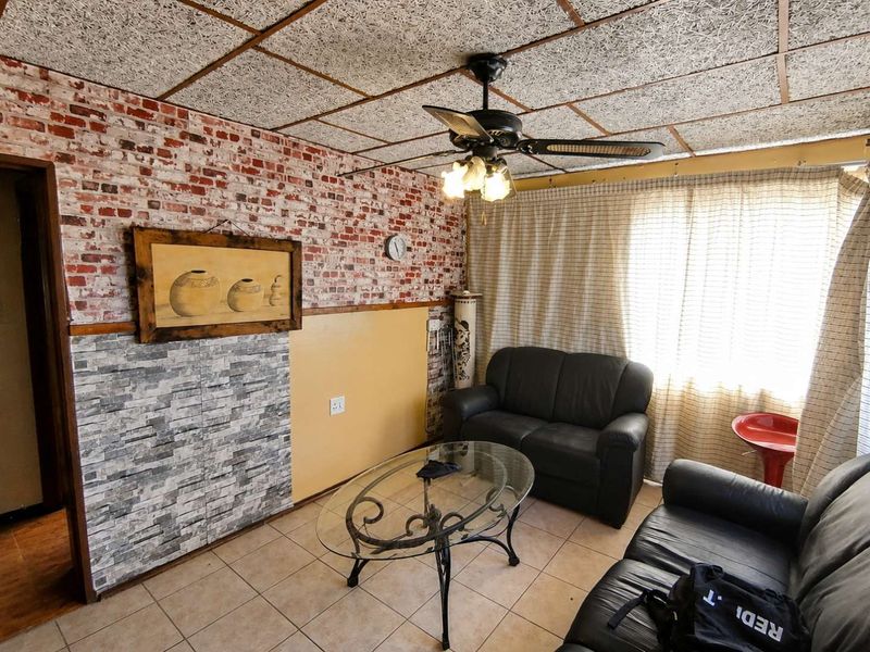 Living room featuring tiled flooring, a ceiling fan, and a combination of brick-effect and stone-effect wall finishes.