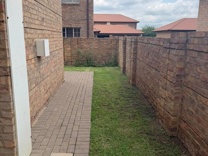 A side garden area featuring a paved walkway, a small lawn, and a brick boundary wall.