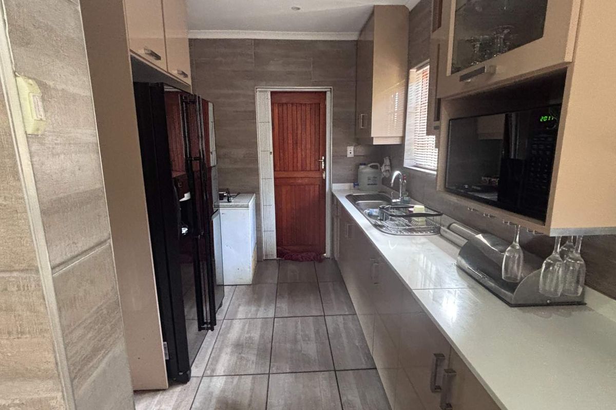 A functional galley-style kitchen featuring built-in cabinetry, stone countertops, a double sink, and tiled flooring with direct access to an exterior door.
