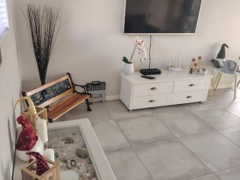 A bright living room featuring large format neutral floor tiles and a wall-mounted television setup.