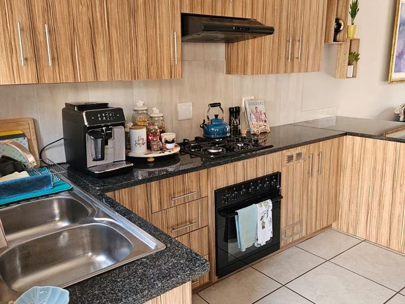 A functional kitchen featuring wood-grain laminate cabinetry, granite countertops, a gas hob with extractor fan, and durable ceramic floor tiles.