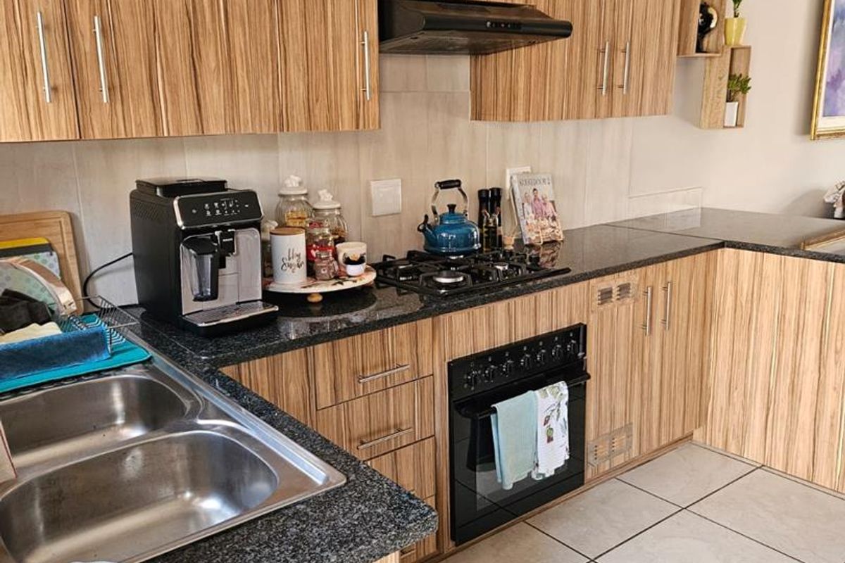A functional kitchen featuring wood-grain laminate cabinetry, granite countertops, a gas hob with extractor fan, and durable ceramic floor tiles.