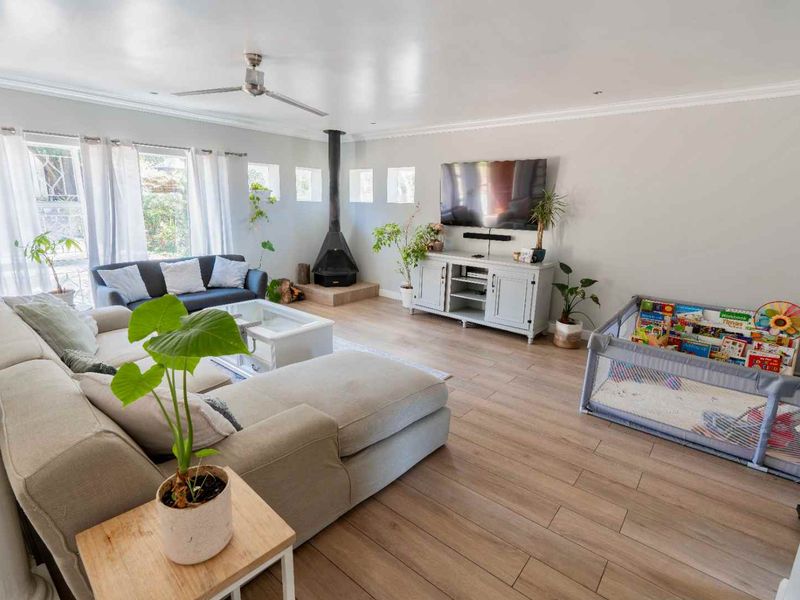 Spacious living room featuring light-toned laminate flooring, a modern wood-burning fireplace, and a ceiling fan, creating a comfortable and inviting atmosphere.