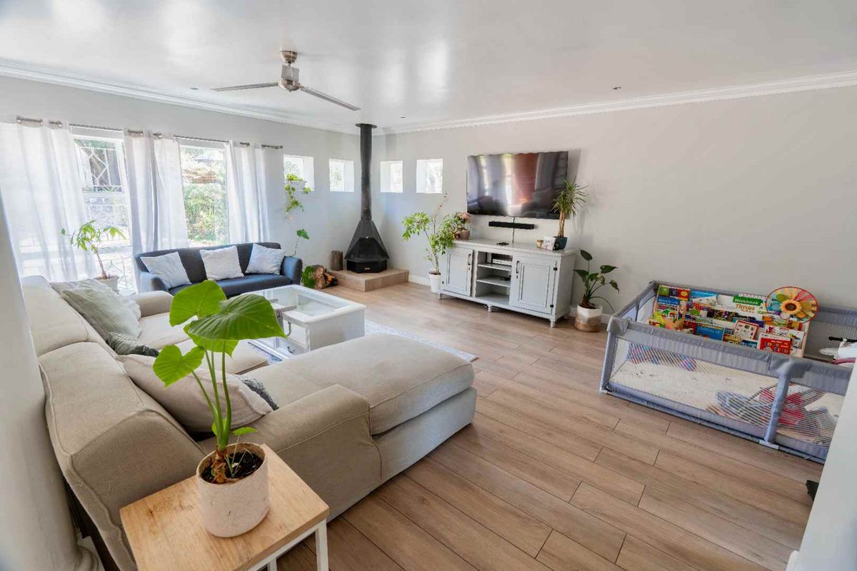 Spacious living room featuring light-toned laminate flooring, a modern wood-burning fireplace, and a ceiling fan, creating a comfortable and inviting atmosphere.