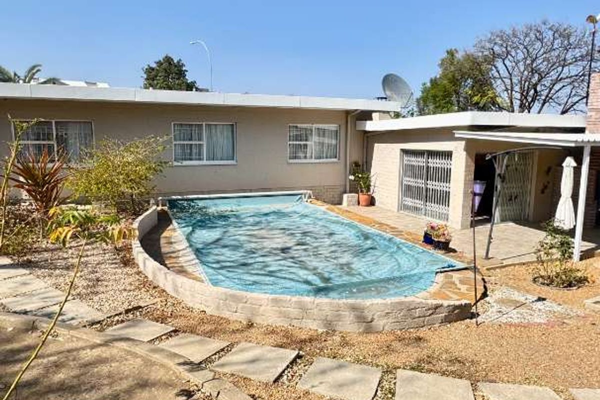 Outdoor pool area featuring a swimming pool with a cover, adjacent paved patio, and low-maintenance garden landscaping.