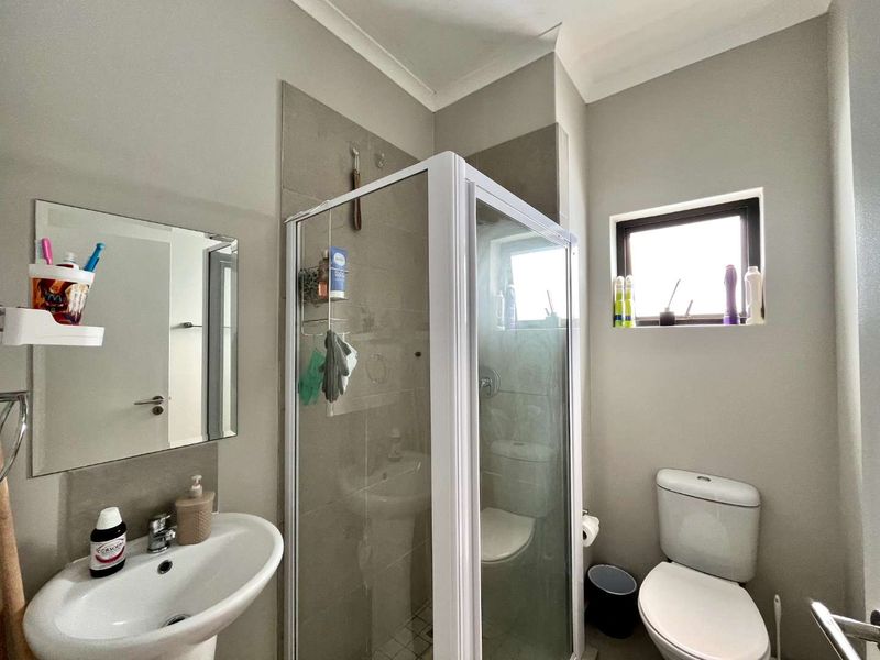 A functional bathroom featuring a pedestal basin, a glass-enclosed shower with tiled splashback, and a standard toilet.