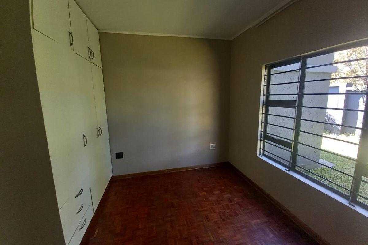 A vacant bedroom featuring classic parquet flooring, built-in storage cupboards, and a window fitted with security bars.