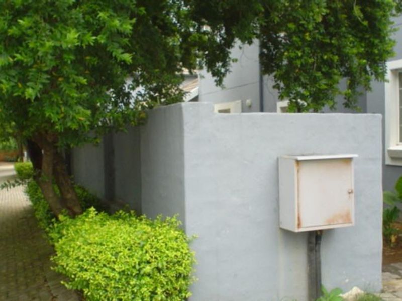 Front exterior view of the townhouse featuring a paved driveway, boundary wall, and external utility box.
