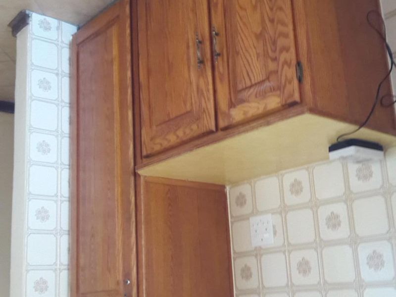 A kitchen area featuring dated wooden cabinetry and patterned wall tiles, requiring modernization to improve the aesthetic appeal of the space.