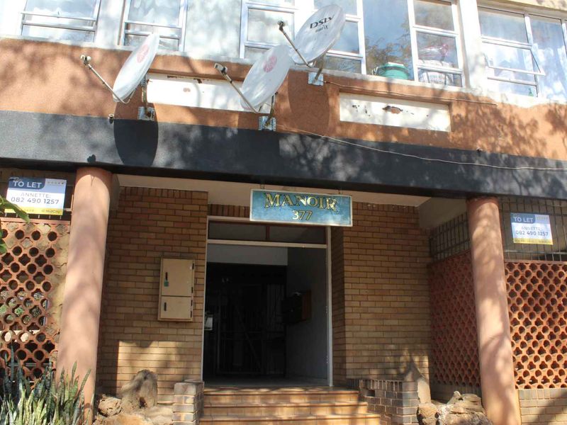 Front entrance of Manoir 377 apartment building featuring brick facade, concrete columns, and decorative breeze block screens.