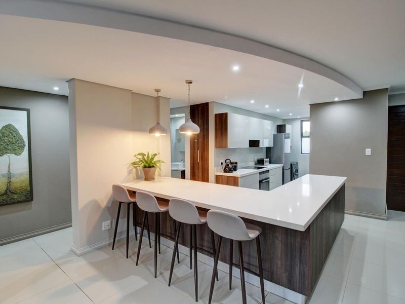 Modern open-plan kitchen featuring a large island with quartz countertops, sleek cabinetry, recessed lighting, and a contemporary drop ceiling design.