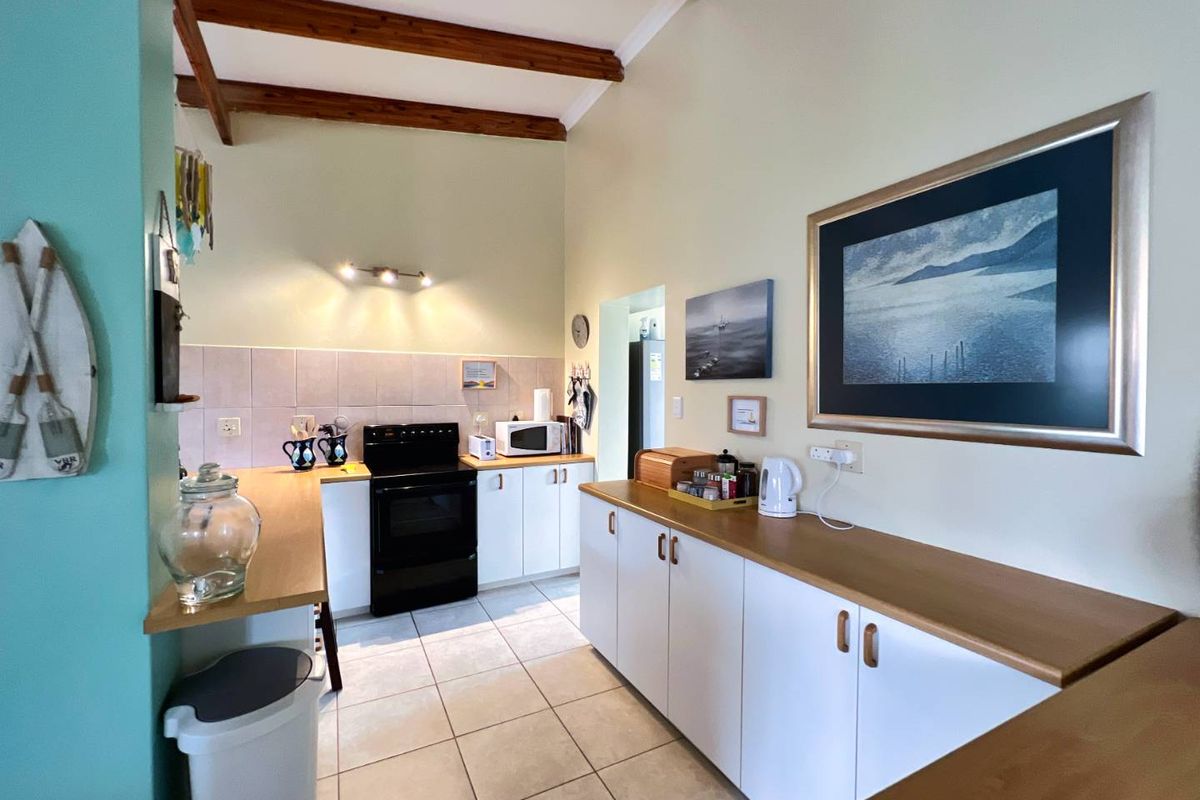 A functional kitchen featuring white cabinetry, wooden countertops, tiled flooring, and exposed timber ceiling beams.