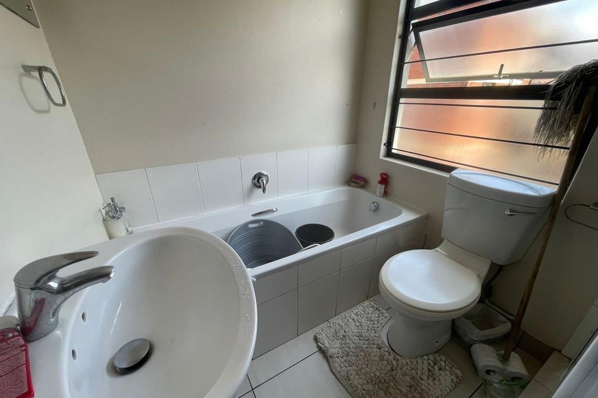 A functional bathroom featuring a built-in bathtub, pedestal basin, and toilet, with tiled flooring and a window providing natural light.