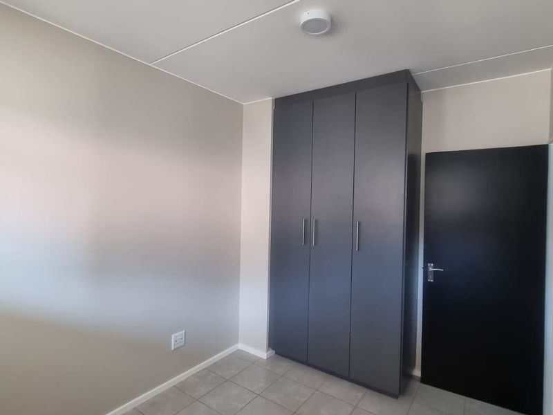 A clean, empty bedroom featuring neutral wall tones, tiled flooring, and a modern dark grey built-in wardrobe.