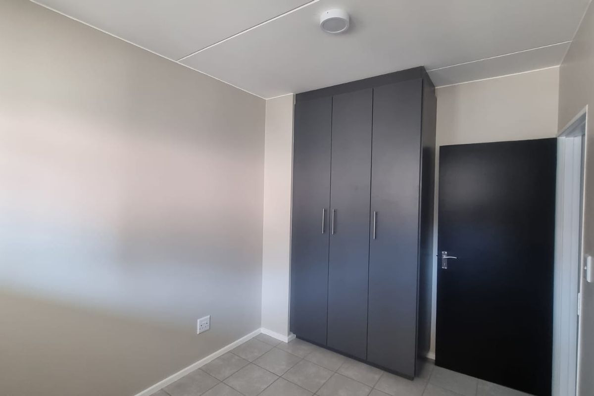 A clean, empty bedroom featuring neutral wall tones, tiled flooring, and a modern dark grey built-in wardrobe.