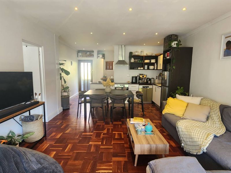 Open-plan living and dining area featuring classic parquet flooring, recessed lighting, and a functional kitchen with built-in cabinetry and stainless steel extractor.
