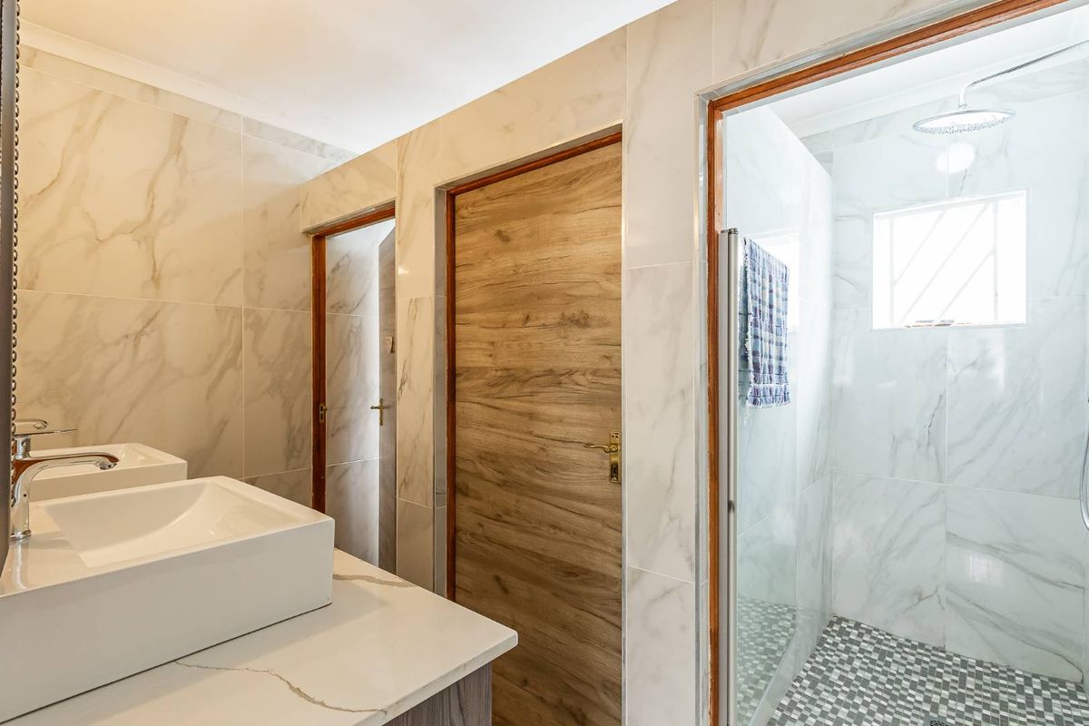 Modern bathroom featuring a double vanity with marble-look tiling, a walk-in shower with a rainfall showerhead, and contemporary wood-grain doors.