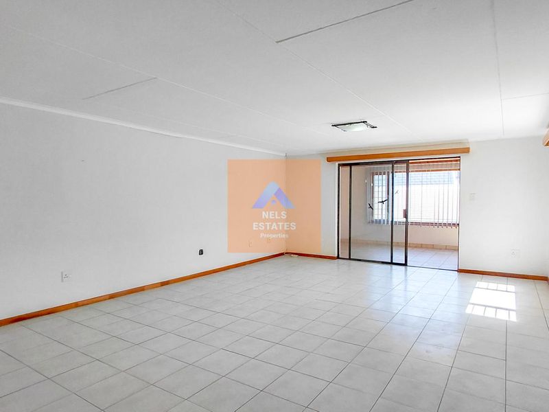 Spacious, empty living area featuring neutral tiled flooring and a sliding glass door leading to an outdoor space.