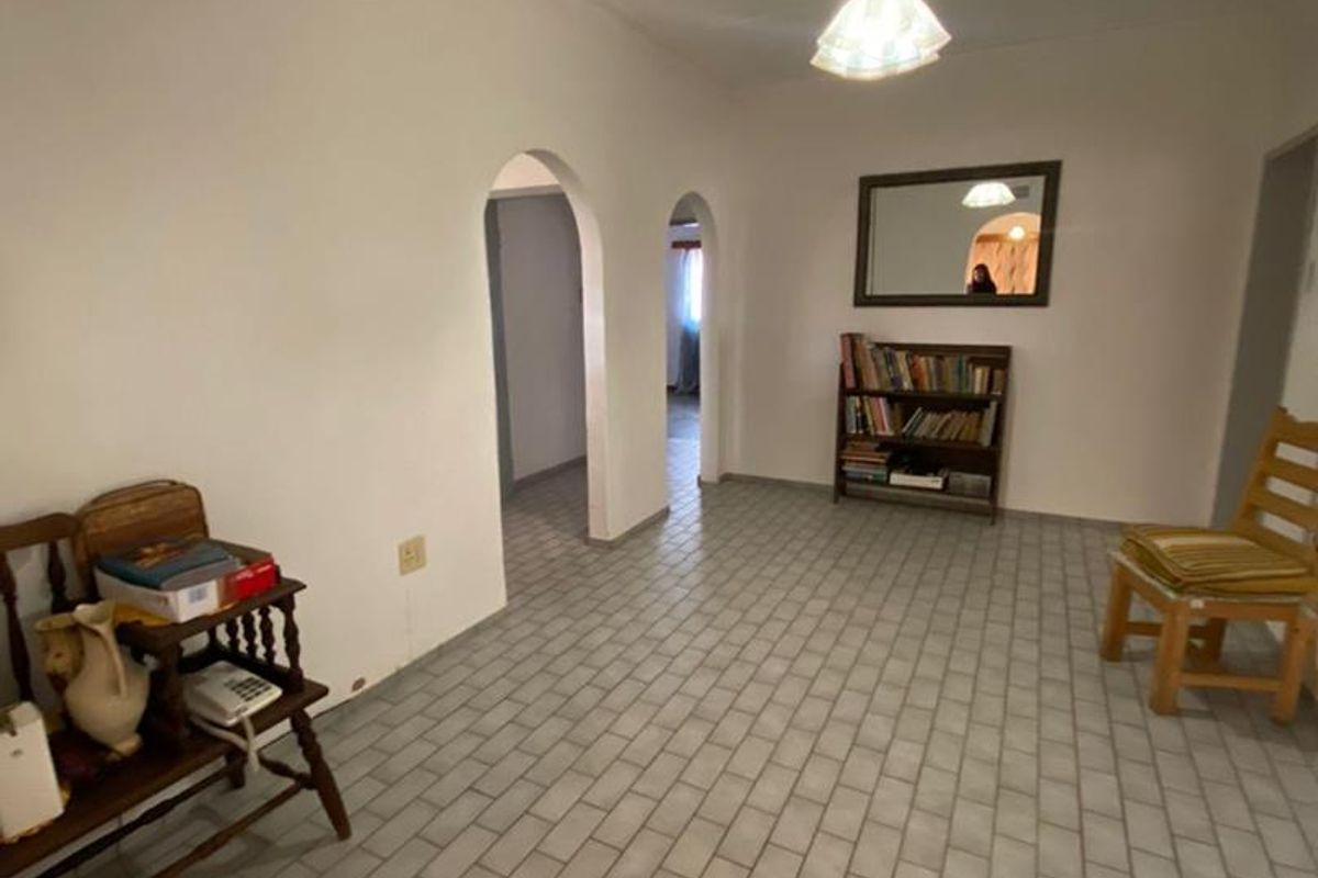 A spacious living area featuring tiled flooring, arched doorways leading to adjacent rooms, and a central pendant light fixture.