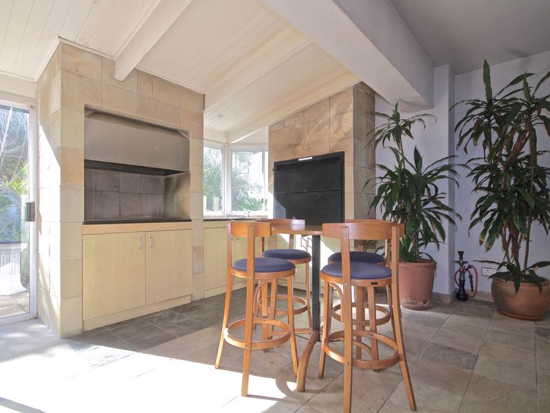Covered patio area featuring a built-in braai, stone cladding, and stone tile flooring, providing a functional space for outdoor entertaining.