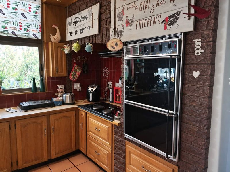 A traditional kitchen featuring timber cabinetry, a built-in double oven, electric hob, and a distinctive brick feature wall with tiled splashbacks.