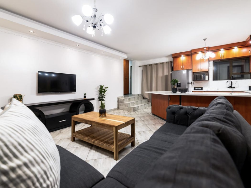 Spacious open-plan living area featuring a modern kitchen with wood-finish cabinetry, a central island, and tiled flooring throughout.