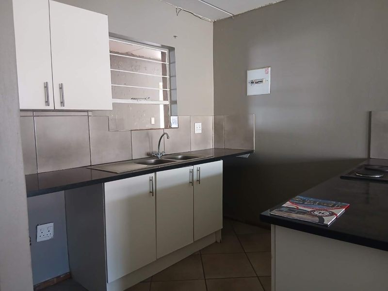A functional kitchen featuring built-in cabinetry, a double sink, tiled backsplash, and dark countertops, providing a clean and practical workspace.