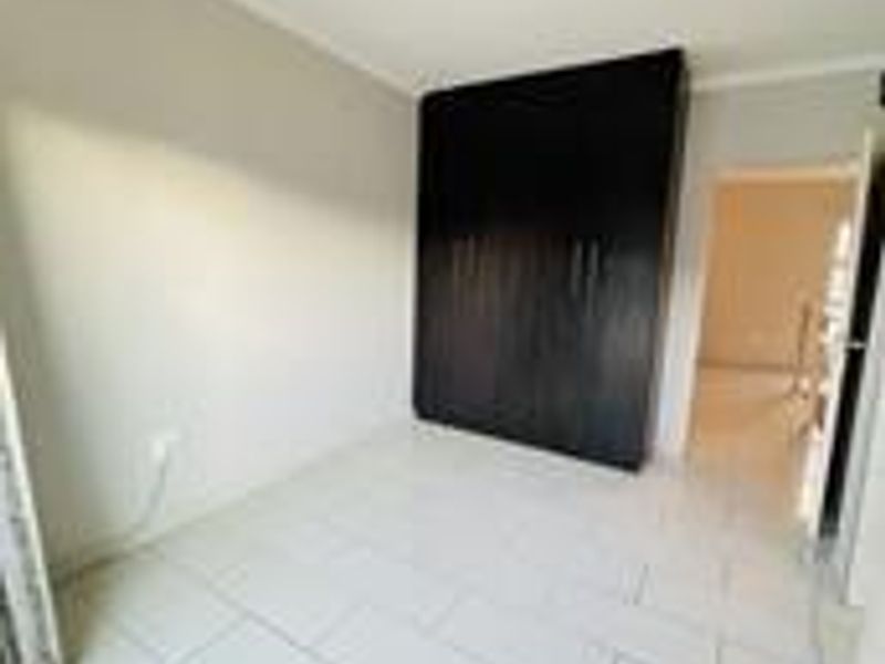 A clean, empty bedroom featuring neutral tiled flooring and a dark wood built-in wardrobe.