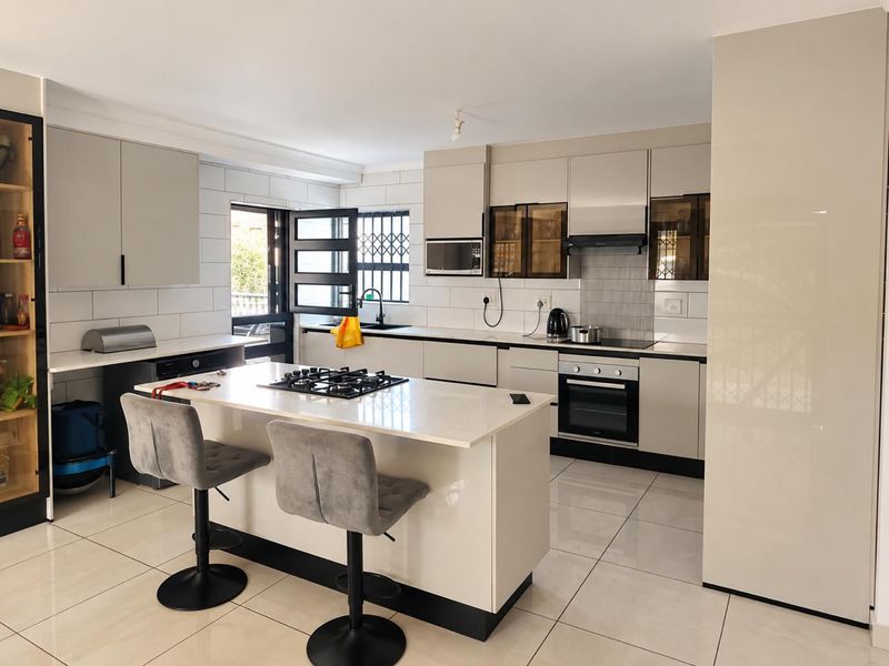 Modern kitchen featuring a central island with gas hob, sleek cabinetry, built-in oven, microwave, and high-gloss tiled flooring.