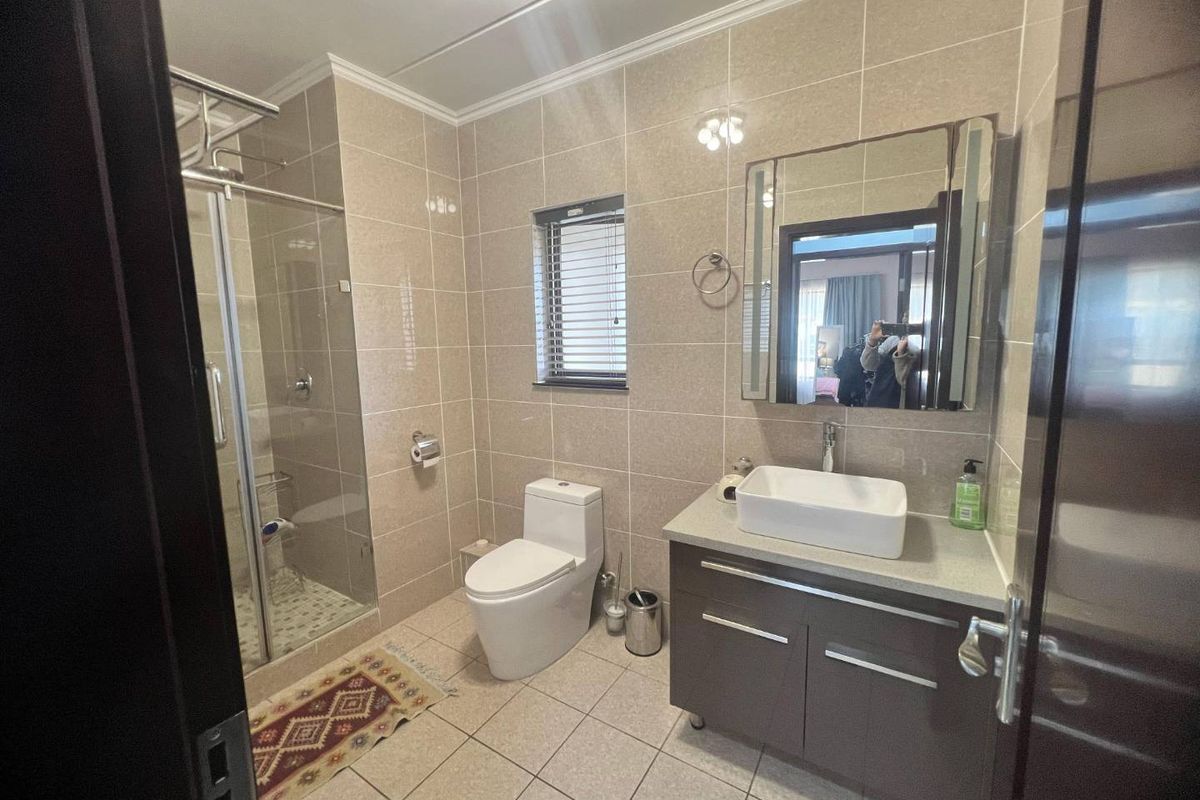 Modern bathroom featuring a glass shower enclosure, wall-mounted toilet, vanity cabinet with vessel sink, and neutral floor-to-ceiling wall tiles.