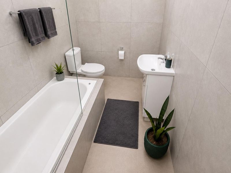 Modern bathroom featuring a bathtub with a glass screen, a vanity basin, and neutral floor-to-ceiling tiling.