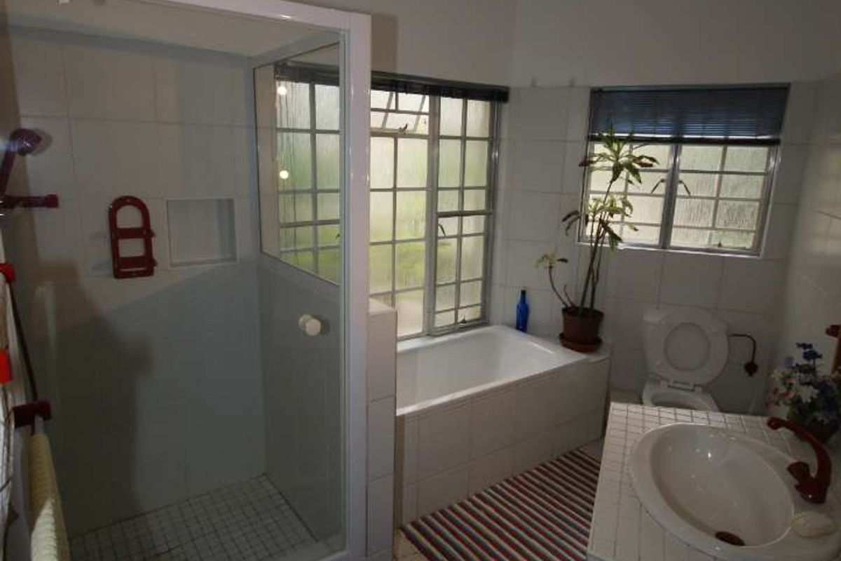 A functional bathroom featuring a glass-enclosed shower, a built-in bathtub, and a tiled vanity with a basin.
