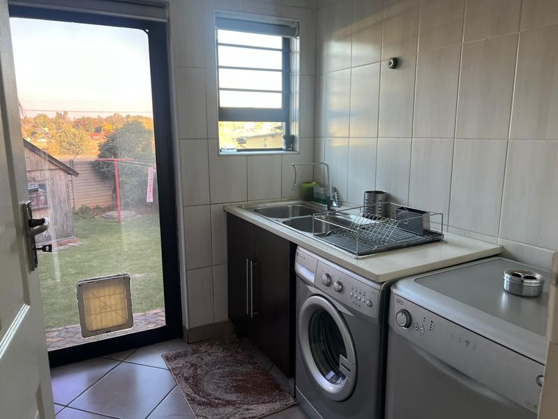 Functional laundry room featuring tiled walls and flooring, built-in cabinetry with a stainless steel sink, and direct access to the rear garden.