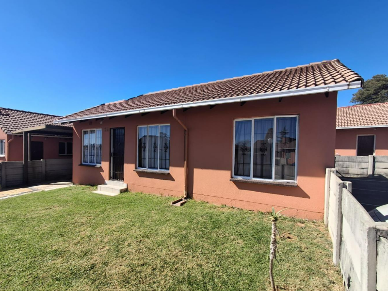 A well-maintained single-story residential house featuring a tiled roof, security gates, and a neat front lawn with precast boundary walling.